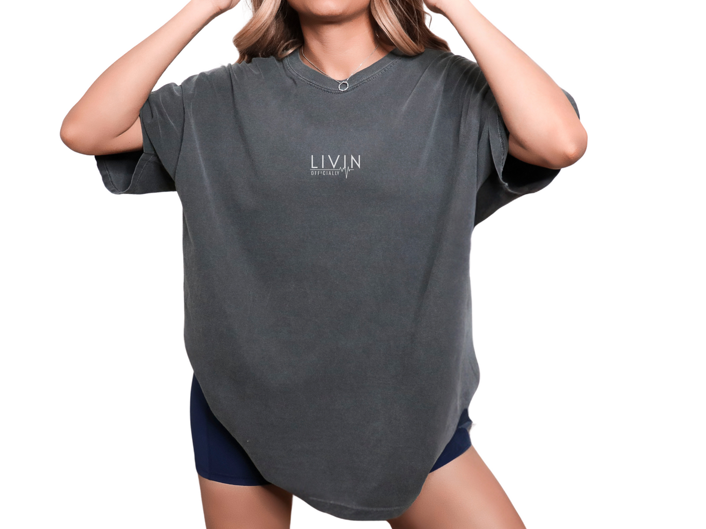 A person wearing a charcoal gray, oversized boxy t-shirt with the text 'LIVIN' and ECG sign on the chest, paired with biker shorts.